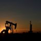 FILE PHOTO: A pump jack operates in front of a drilling rig at sunset in an oil field in Midland